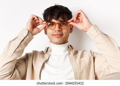 Close-up Of Stylish Hipster Guy Trying Eyewear At Optician Store, Put On Glasses And Smiling, Standing On White Background