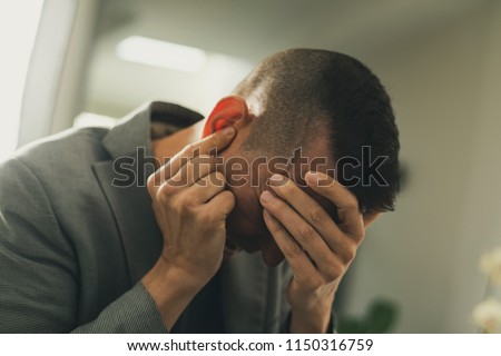 closeup of a suffering caucasian man with one hand in his head and the other hand covering his ear