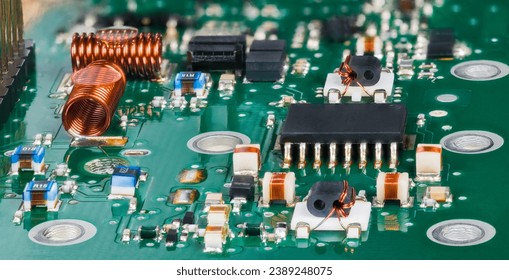 Closeup of surface mounted electronic components in radio-frequency circuits of TV tuner. Semiconductor microchip and air core coils with various small inductors, capacitors or resistors on green PCB.