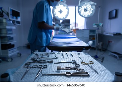 Close-up of surgical instruments arranged on table in operating room while African-american male surgeon putting gloves on background. Shot in real medical hospital with doctors nurses and surgeons in