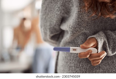 Closeup, surprise and hands of a woman with a pregnancy test for husband at home. Showing, back and a person holding and hiding a tool with pregnant results during announcement to a man in a house - Powered by Shutterstock