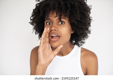 Close-up Of Surprised African American Woman Telling Rumor. Face Of Young Woman Wearing White Top Looking At Camera And Whispering. Gossiping And Rumor Concept