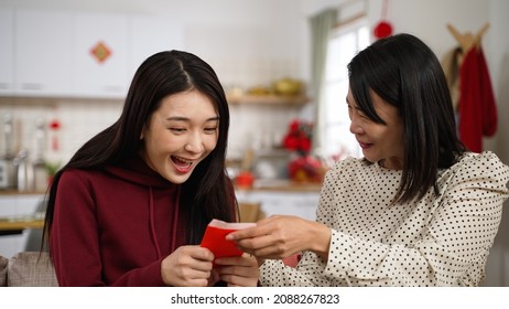 Closeup Of Surprised Daughter Giving Her Mother A Hug With Smiling Face While Receiving Red Envelope Lucky Money During Spring Festival Chinese New Year At Home