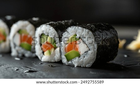 Close-up of sushi rolls with seaweed, rice, salmon, avocado, and cream cheese on a dark slate surface.