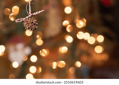 Close-up of a sweet gum seed pod ornament tied with a red and white string, hung on a holiday tree, bokeh background. - Powered by Shutterstock