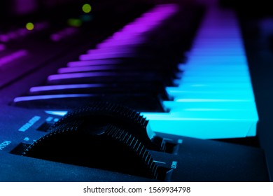 Closeup Of Synthesizer Keyboard With Focus On Pitch And Modulation Wheels In Dark Ambient Illuminated By Pink And Blue Light. Music And Instruments