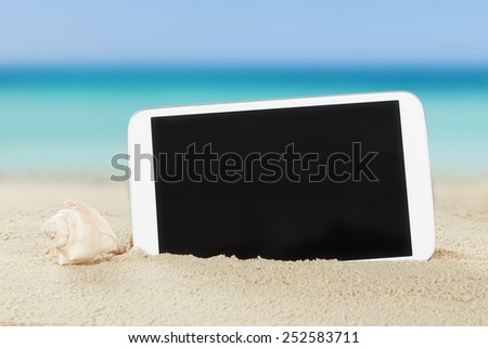 Closeup of tablet computer and shell on sand at beach
