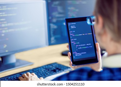 Closeup Tablet Screen With Conceptual Program Code About Healthy Lifestyle In Male Hand. Programmer Developer Is Writing Software On Multiple Computer Monitors At Home Office. Devices For Working.