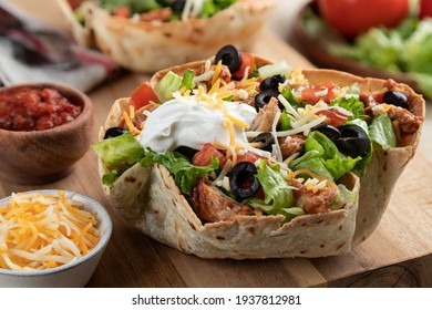 Closeup of a taco salad made with chicken, lettuce, tomato, black olives, cheese and sour cream in a tortilla shell