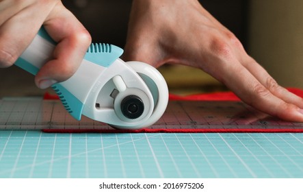 Closeup of a tailor cutting red fabrics using roller knife. Tools for sewing concept. - Powered by Shutterstock