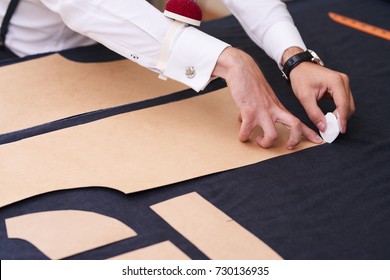 Closeup of tailors table with male hands tracing fabric making pattern for clothes in traditional atelier studio - Powered by Shutterstock