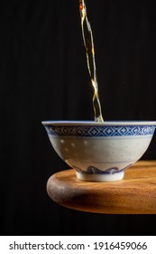 Close-up Of Tea Falling Into China Cup, On Wooden Table, Black Background, Vertical, With Copy Space