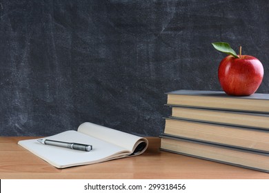 Closeup of a teachers desk with books, paper and pen and a red apple in front of a chalkboard. Horizontal format with copy space.  - Powered by Shutterstock