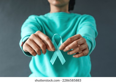 Close-up teal awareness ribbon holded by woman hands to support cancer survivor. Ovarian Cancer month, cervical cancer day.  - Powered by Shutterstock