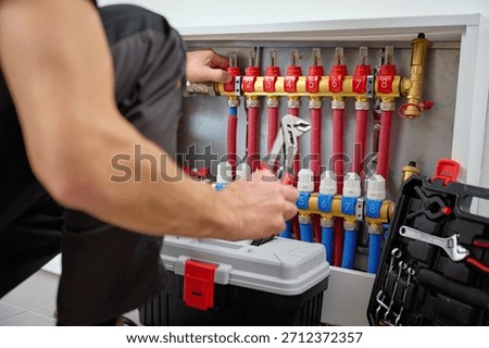 Close-up of technician adjusting control knobs on underfloor heating manifold with with red and blue pipes in circuits. Concept of heating system maintenance and plumbing service