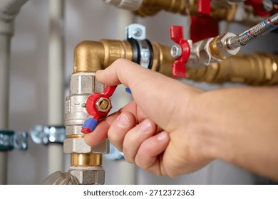 Close-up of technician hand adjusting valve on heat pump piping system with pipes and fittings. Concept of heating maintenance and plumbing service