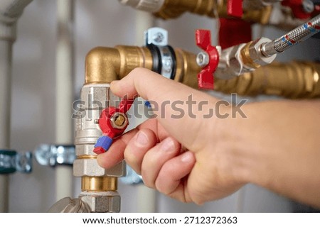 Close-up of technician hand adjusting valve on heat pump piping system with pipes and fittings. Concept of heating maintenance and plumbing service