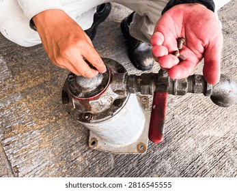 Close-up of a technician reinstalling bolts while reassembling an industrial oil filter during preventive maintenance at an oil and gas facility. The image represents mechanical servicing, equipment inspection, and industrial maintenance operations.