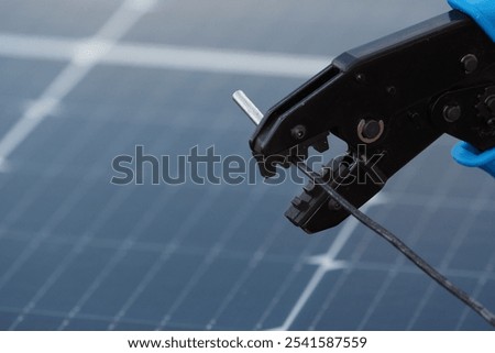 Close-up of a technician using a crimping tool to connect wires on a solar panel during installation at a renewable energy site.