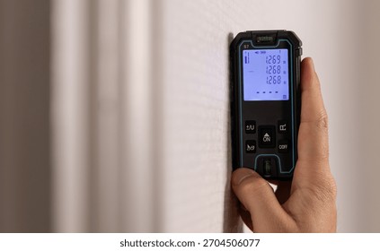 Close-up of a technician using a laser rangefinder in an apartment.