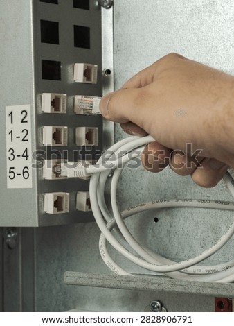 Close-up of a technician's hand plugging a white RJ45 ethernet patch cord cable into a network patch panel socket inside a server cabinet. High-speed internet connection, local area network (LAN), and IT infrastructure concept.