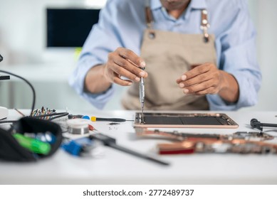 Close-up of technician's hands using screwdriver to repair damaged tablet in electronics repair shop, surrounded by tools and components