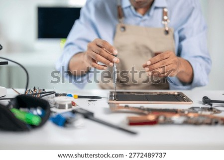 Close-up of technician's hands using screwdriver to repair damaged tablet in electronics repair shop, surrounded by tools and components