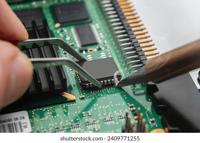 Close-up of a technician's hands in a workshop. The repairer is soldering an IC in a PLCC package to the circuit board of an electronic device.