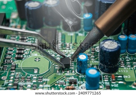 Close-up of a technician's hands in a workshop. The repairer is soldering an IC in a SOIC package to the circuit board of an electronic device.