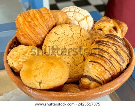 Close-up of a tempting assortment of Mexican sweet breads, featuring conchas, pastries, and muffins, presented in a traditional clay dish.