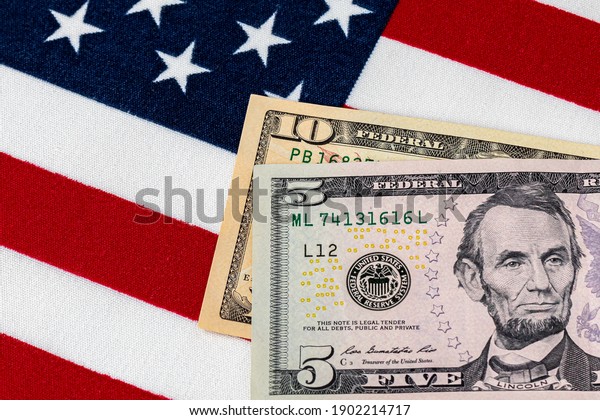 Closeup of ten and\
five dollar bills with American flag.  Concept of 15 dollar federal\
minimum wage increase