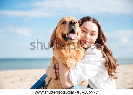 Closeup of tender smiling young woman hugging her dog on the beach