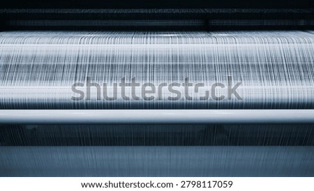 Close-up of a textile weaving machine in operation. Fabric threads move through the machine's rollers smoothly.  woven material has light, textured appearance
