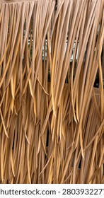 Close-up texture of artificial thatch straw roof background.

A vertical close-up shot of artificial thatch straw or synthetic palm leaf roof texture. The image showcases layers of long, slender light brown and beige plastic grass blades hanging vertically, designed to mimic a traditional tropical tiki hut or beach resort roofing. Captured under bright daylight, highlighting the repetitive linear pattern and rustic holiday vibe. Perfect for summer travel backdrops, exotic resort branding, and tropical abstract design concepts.
