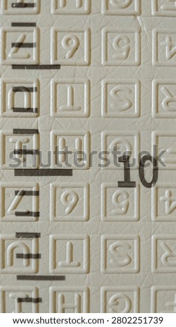 Close-up texture of a beige surface with embossed alphabet letters and a printed black number ten.