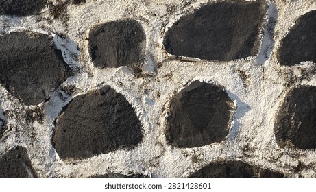 Close-up texture of a dark stone wall with rough white mortar filling the gaps, showing natural ruggedness and weathered detail in daylight
