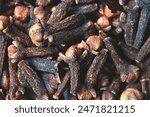A close-up texture of freshly dried clove spices scattered on the ground. Cloves serve as a dried herb for food flavoring and natural medicine. Dry Organic Clove Spice.
