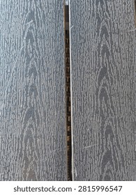 Close-up texture of grey composite decking or wooden planks. The image highlights the vertical grain and grooved texture of weatherproof outdoor flooring material, showing a subtle weathering effect and neutral tones suitable for modern exterior design or architectural backgrounds.