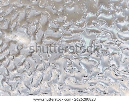 Close-up texture of an iridescent, wavy surface resembling melted plastic or pearlescent material.