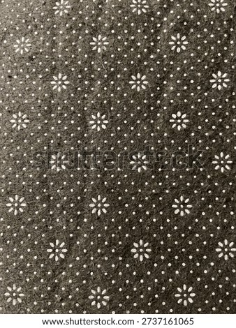 Close-up texture of patterned fabric with small white floral and dot motifs on a dark earthy background. Repeating decorative textile surface suitable for background, wallpaper, or design use.