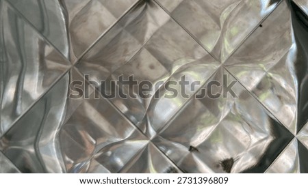 Close-up texture of patterned glass block. Abstract geometric background of translucent glass wall with diamond shapes and light reflections. Silver distorted glass texture background. Macro view of architectural glass brick surface with wavy lines and glossy relief.