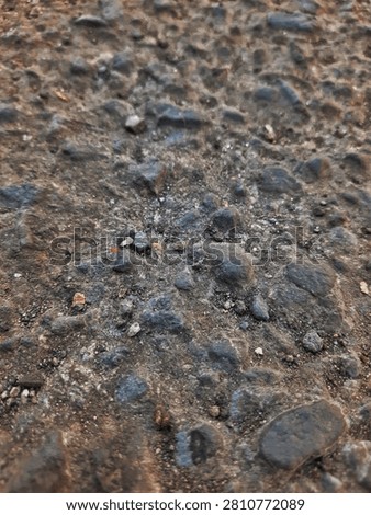 Close-up texture of a rough, weathered gray asphalt road surface with embedded gravel.
