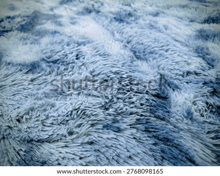 Close-up texture of soft blue and white faux fur rug with wavy fibers.