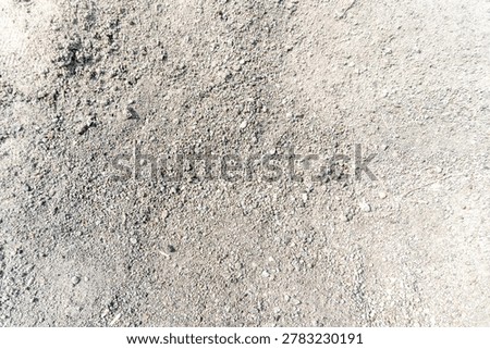 Close-up of a textured surface, possibly composed of fine gravel, sand, or crushed stone. Small, gray pebbles of varying sizes are scattered throughout the surface.