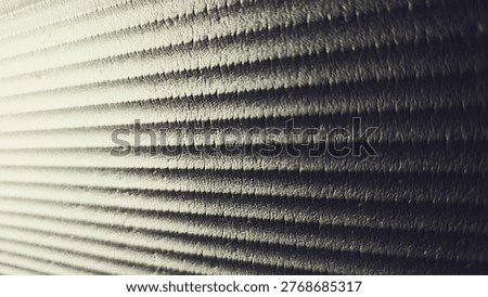 Close-up of a textured surface with repeating horizontal ridges forming a rhythmic linear pattern. The image features a monochrome palette with subtle gradients of light and shadow, enhancing depth and dimension. Fine granular details are visible along the ridges, creating a tactile and slightly rough appearance. The perspective adds a sense of direction and flow across the frame. Abstract composition suitable for backgrounds, texture studies, or minimalist design themes.