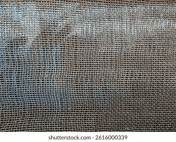 A close-up of a textured window mesh, showcasing a fine, grid-like pattern with a slightly worn or weathered appearance.