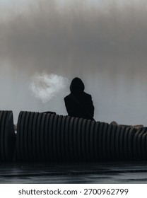 A close-up that emphasizes the visual contrast between the black, indistinguishable hooded figure and the bright, ephemeral cloud of breath vapor. For themes of cold, loneliness, mystery, and mysticis