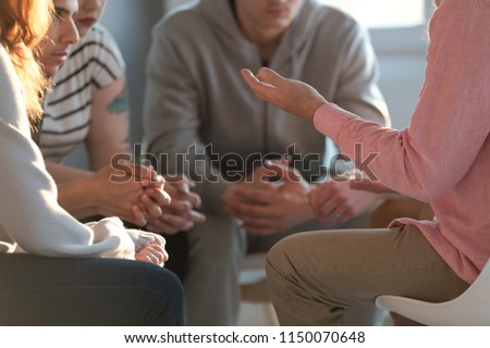 Close-up of a therapist gesticulating while talking to a group of listing teenagers during an educational self-acceptance and motivation meeting.