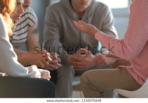 Close-up of a therapist gesticulating while\
talking to a group of listing teenagers during an educational\
self-acceptance and motivation\
meeting.