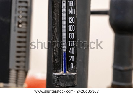 A close-up of a thermometer indicating approximately 100 C in an industrial setting.